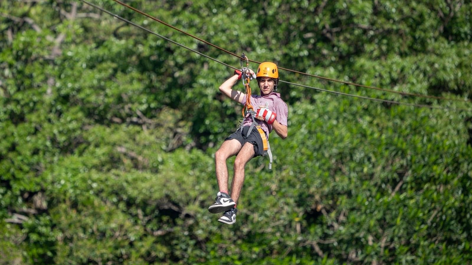 Person wearing yellow helmet zip-lining through lush green forest canopy on adventure travel experience.