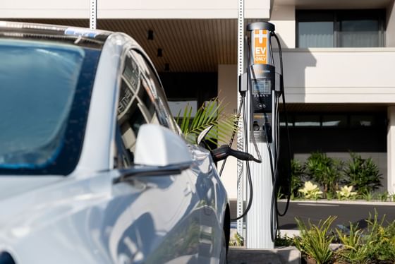 Luxury white electric vehicle charging at the charging station, surrounded by green tropical plants at Maui Coast Hotel