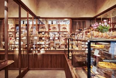 Bakery with wooden shelves and glass cases displaying a variety of breads and pastries in Motto Bakery at Hotel Motto Vienna