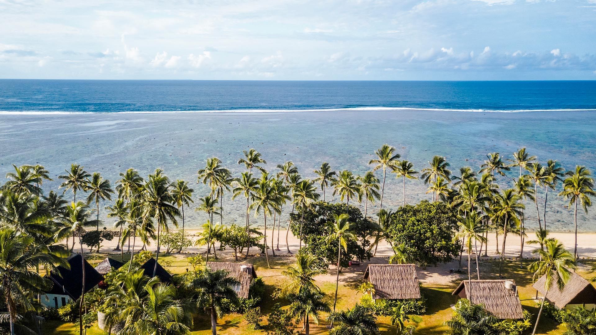 Aerial view of villas by a white sand beach under palm trees surrounding the blue sea at Tambua Sands Beach Resort