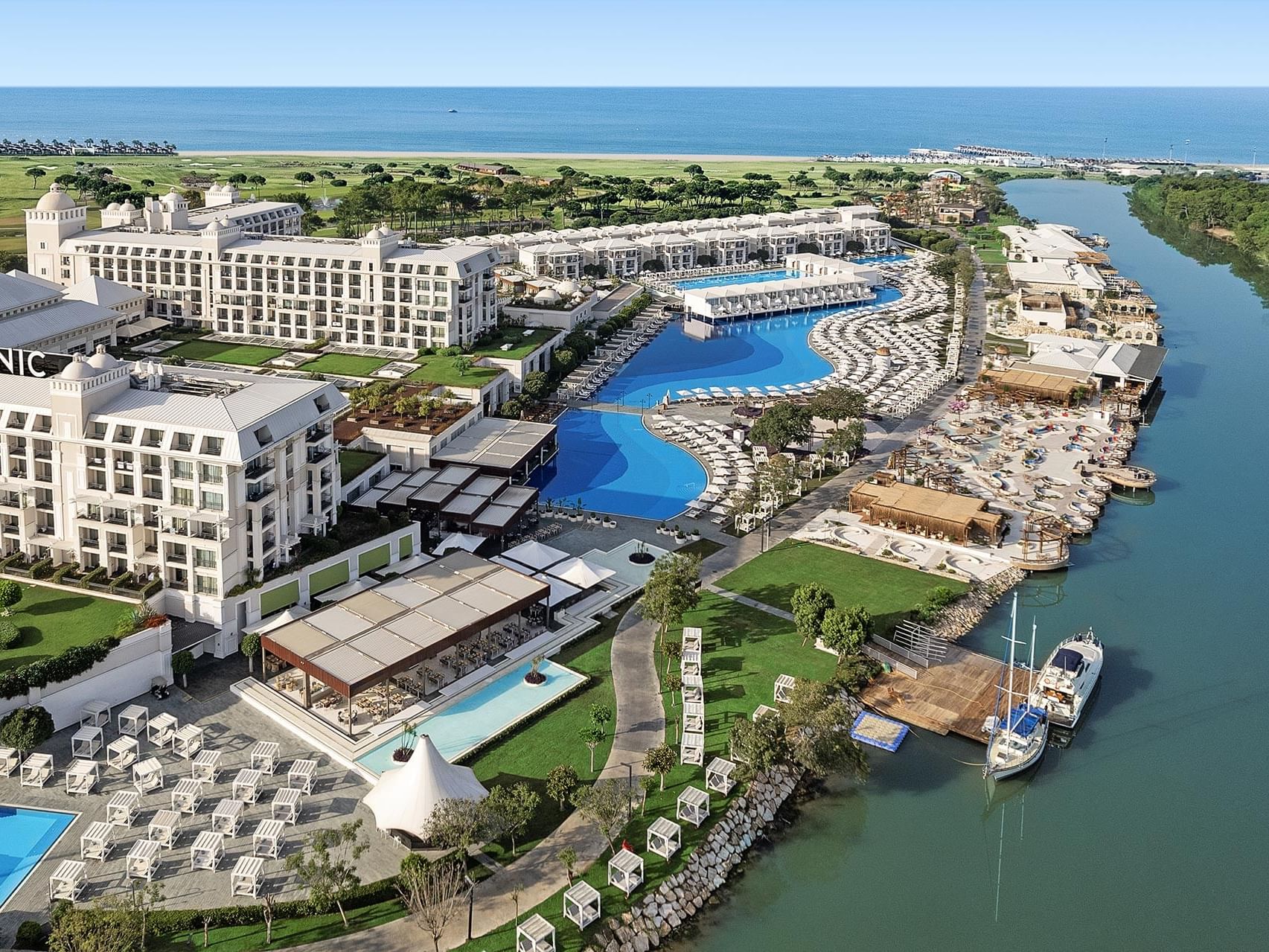Aerial view of Titanic Deluxe Golf Belek with outdoor pool next to the river and greenery