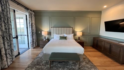King bed with a cushioned headboard & wooden floors in King Room With Balcony at Camp Creek Inn