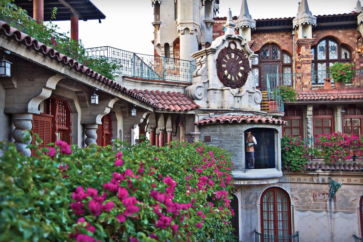 Ornate clock on a stone wall by purple bougainvillea under a tiled roof at Mission Inn Riverside