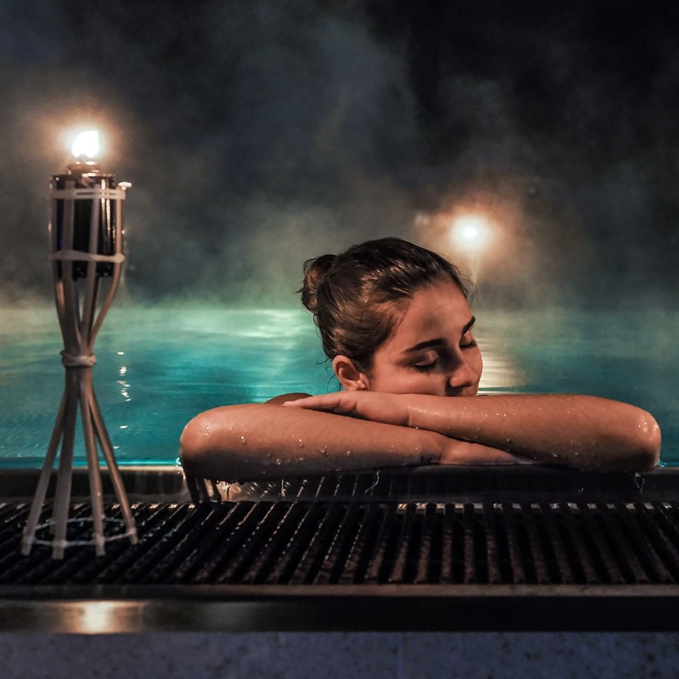 Woman relaxing in a hot tub with a lit torch nearby.