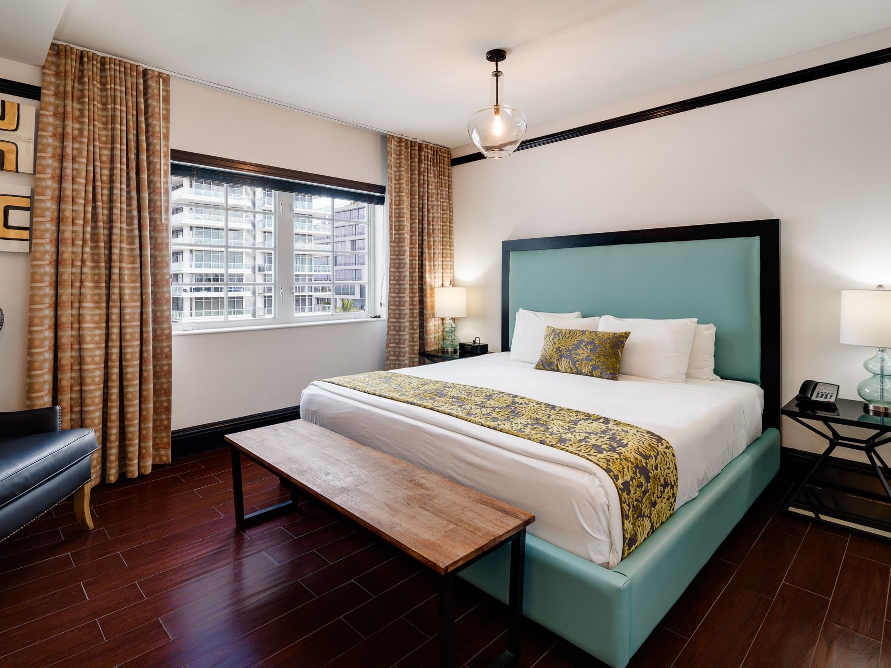 A bedroom with a bed, bench, chair, lamp, and window with curtains.
