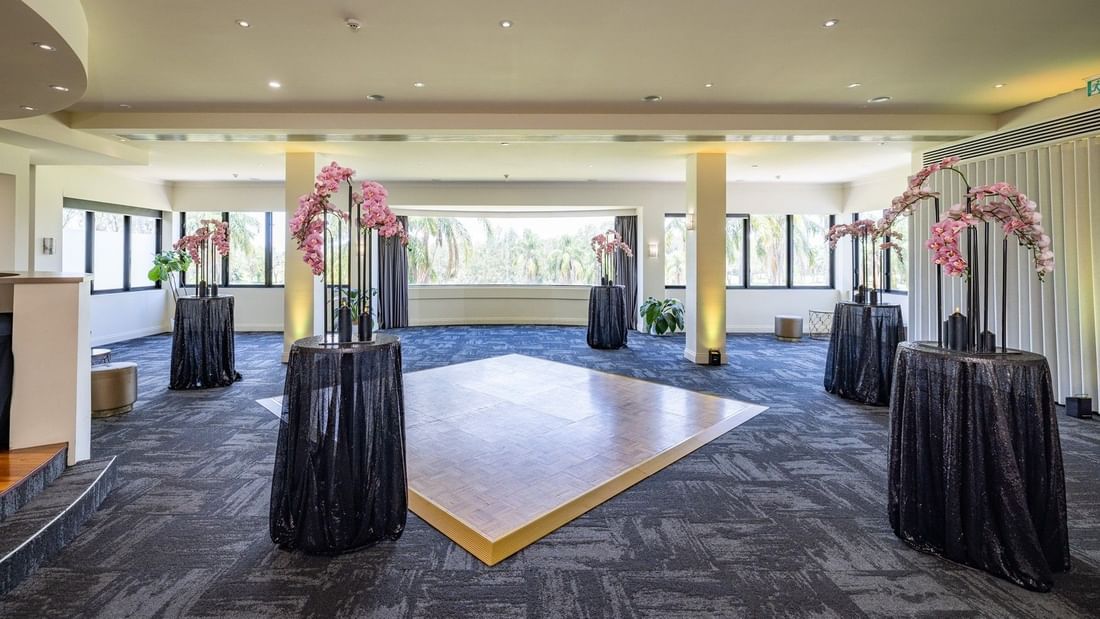 Large room with tables draped in black, floral arrangements, and a central dance floor under soft lighting.