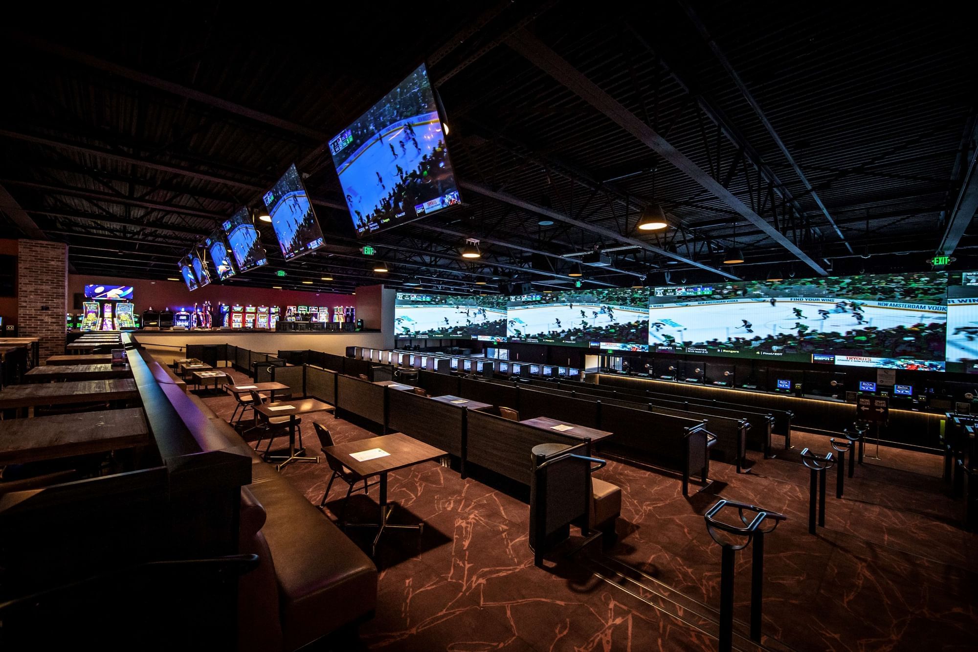 Sportsbook tables and booths by betting screens under hockey displays and hanging ceiling lights at The Brook