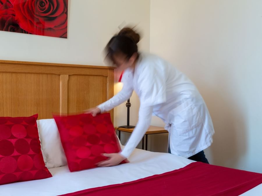 A lady arranging a bed in a room at Hotel Saint-Laurent