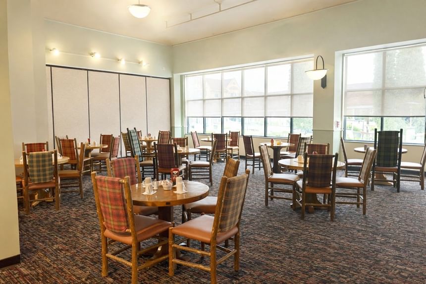 Stagedoor Restaurant hall with plaid wooden chairs, round tables, and large bright windows at Branson Hillside Hotel