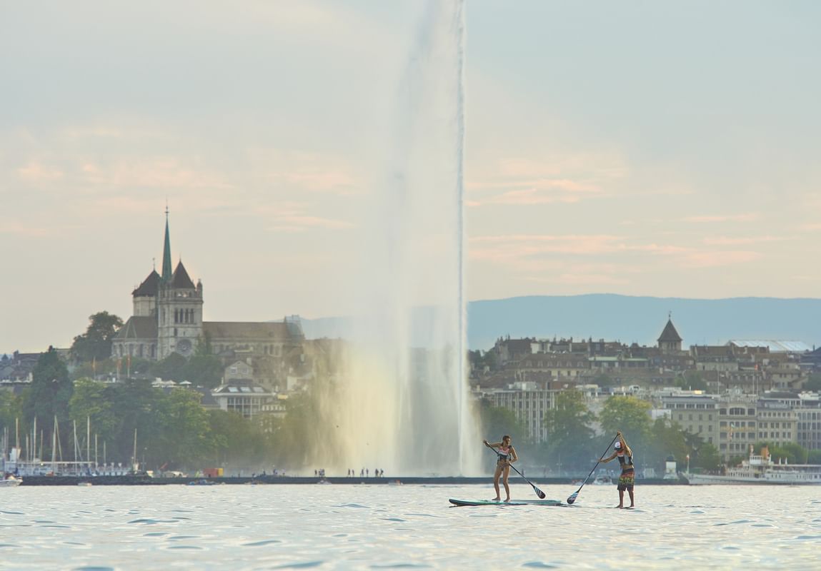 Deux personnes pratiquent le paddle sur le lac Léman avec le Jet d'Eau et la ville en arrière-plan au Warwick Geneva Genève