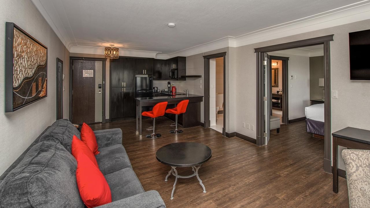 Modern hotel suite with open living area, kitchenette with red bar stools, gray sofa, and wood floors at Coast Calgary University Area Hotel by APA.