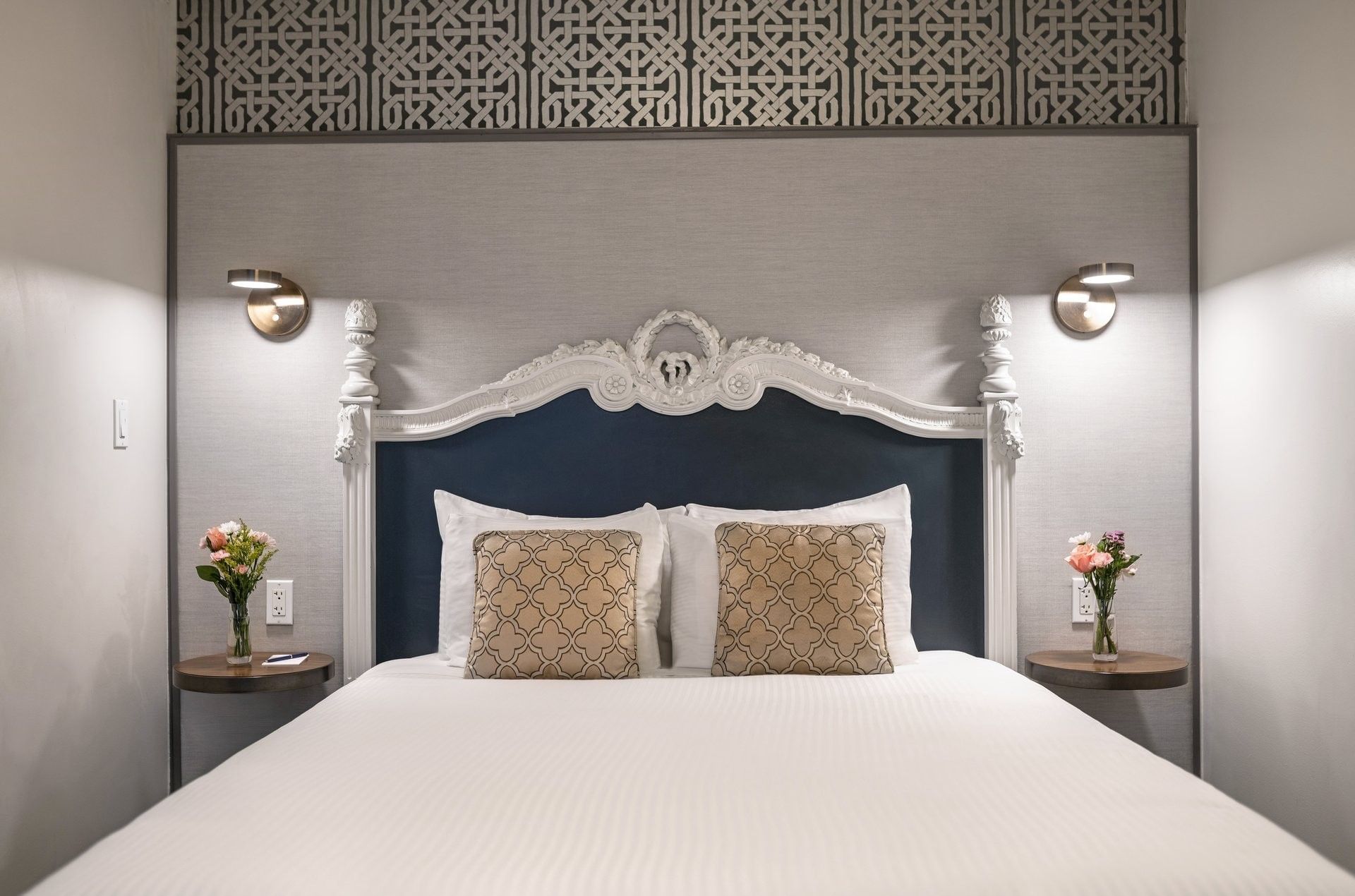 Bed with an ornate headboard by floating nightstands under brass lamps in Suite at Warwick San Francisco