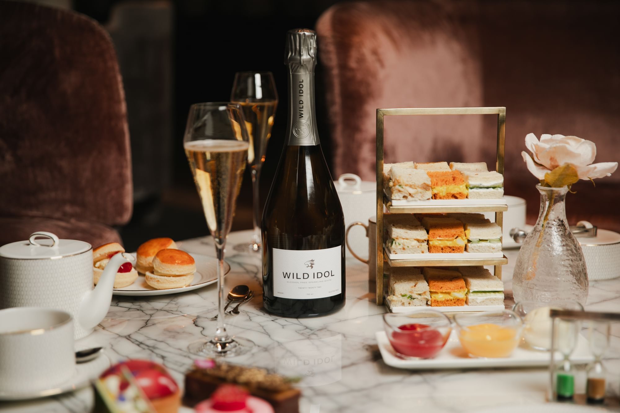 Mesa de chá da tarde com sanduíches, scones e uma garrafa de champanhe Wild Idol no The Londoner Hotel
