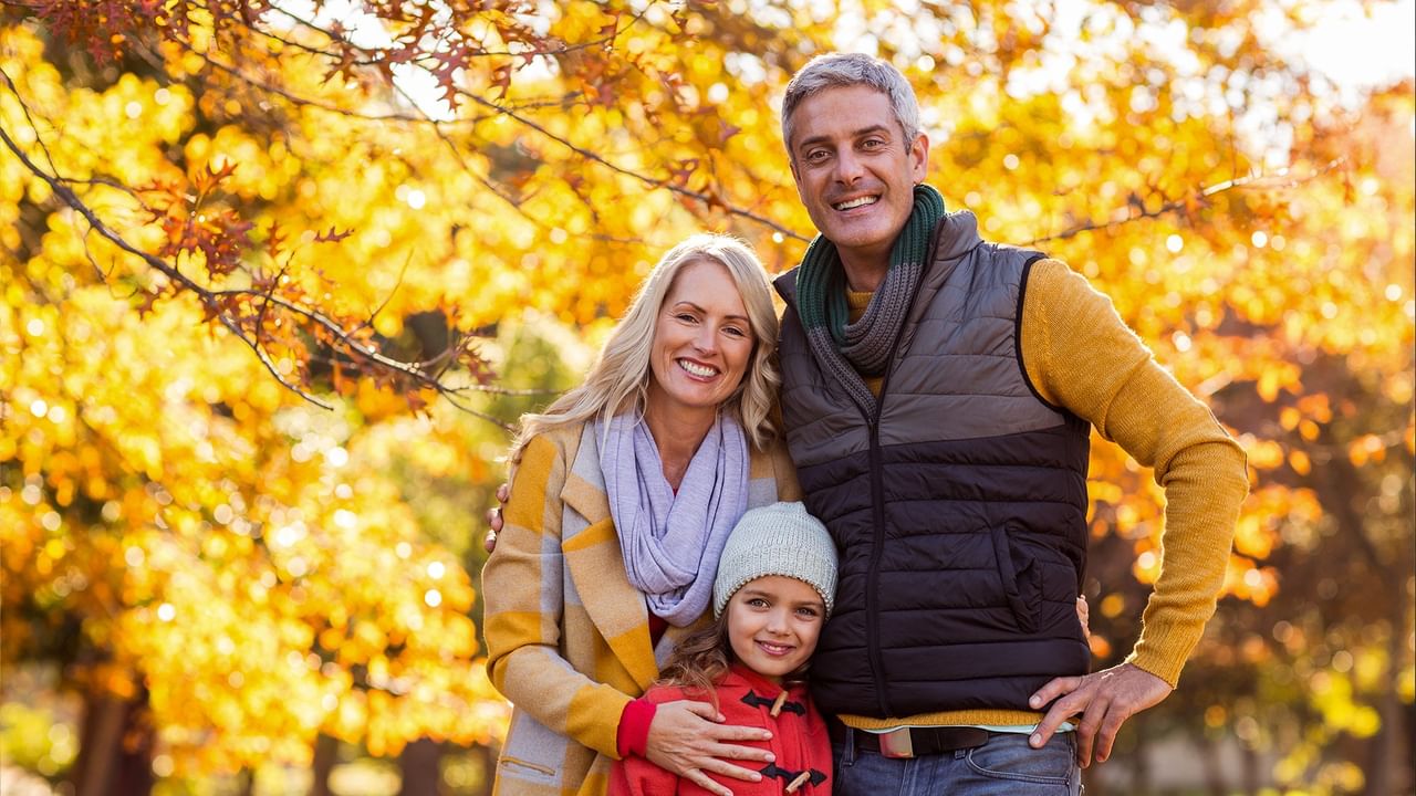 Smiling family of three enjoying autumn outdoors with vibrant golden foliage for Fall Savings.