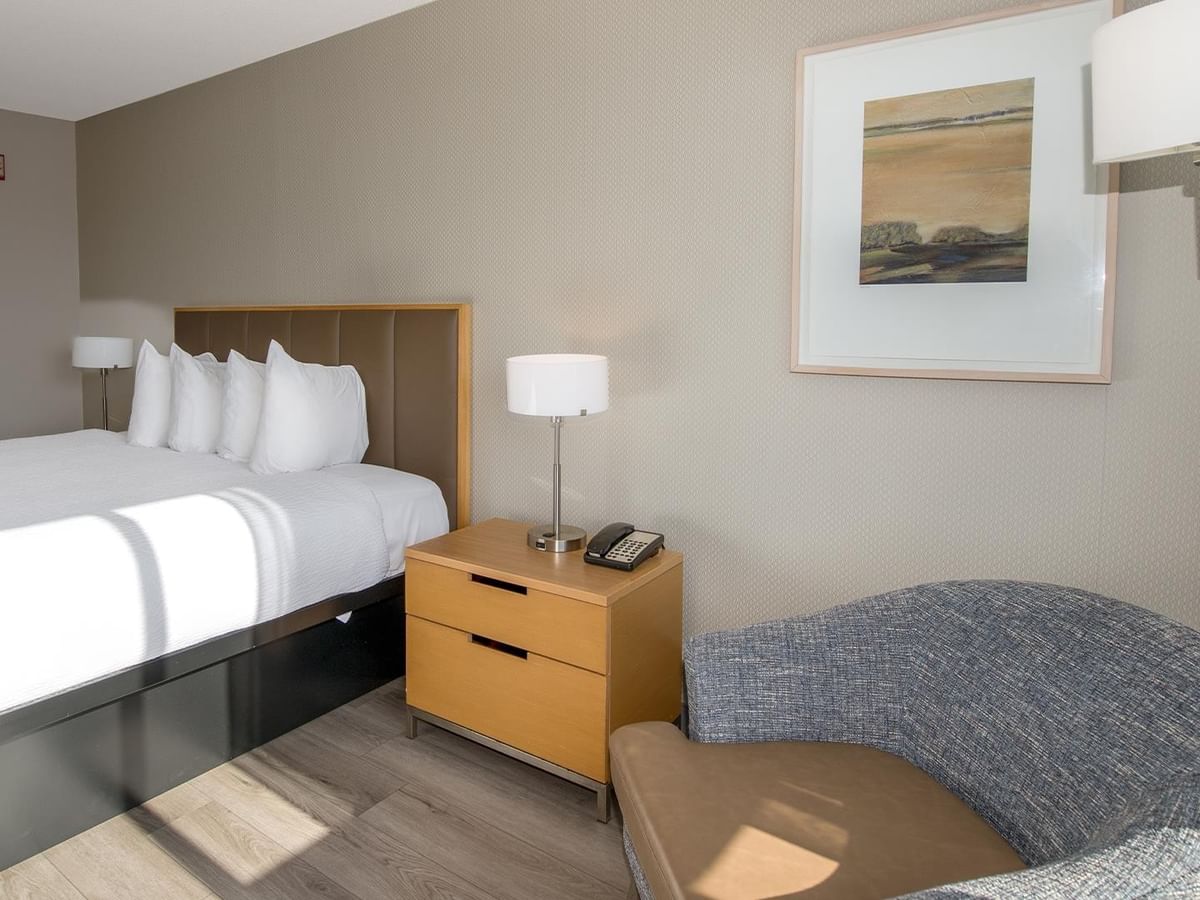 King bed, nightstand, lamp, and chair in a hotel room.