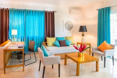 Teal-cushioned sofa and armchairs around a wooden coffee table under a art in Junior Executive Suite at Hotel Montana Haiti