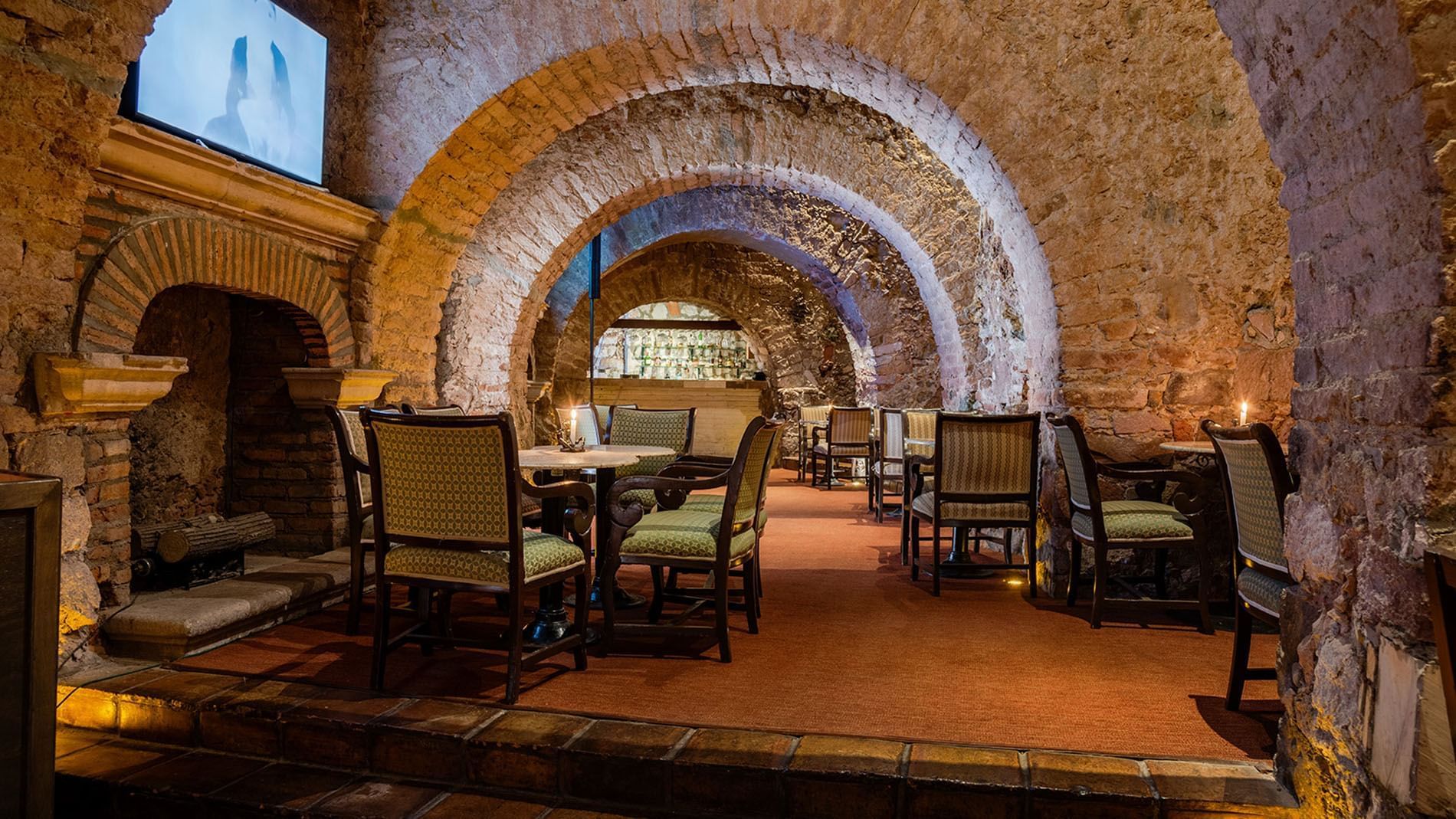 Bar Botarel featuring dramatic stone arches and elegant green patterned chairs at Quinta Real Zacatecas