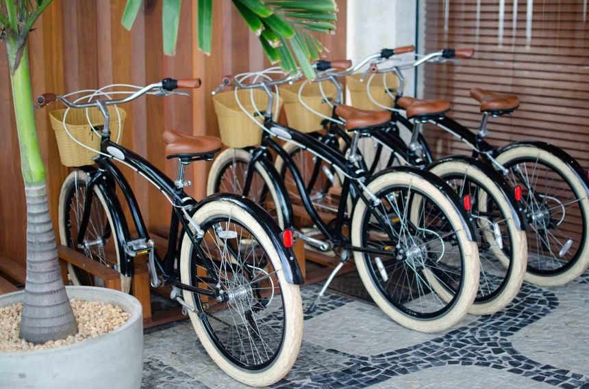 Quatro bicicletas pretas com rodas brancas e cesto oferecidas pelo Janeiro Hotel ao seus hóspedes