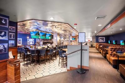 Central bar with blue stools beside padded leather booths under a tin ceiling in ML Steaks & Sports at Miami Lakes Hotel