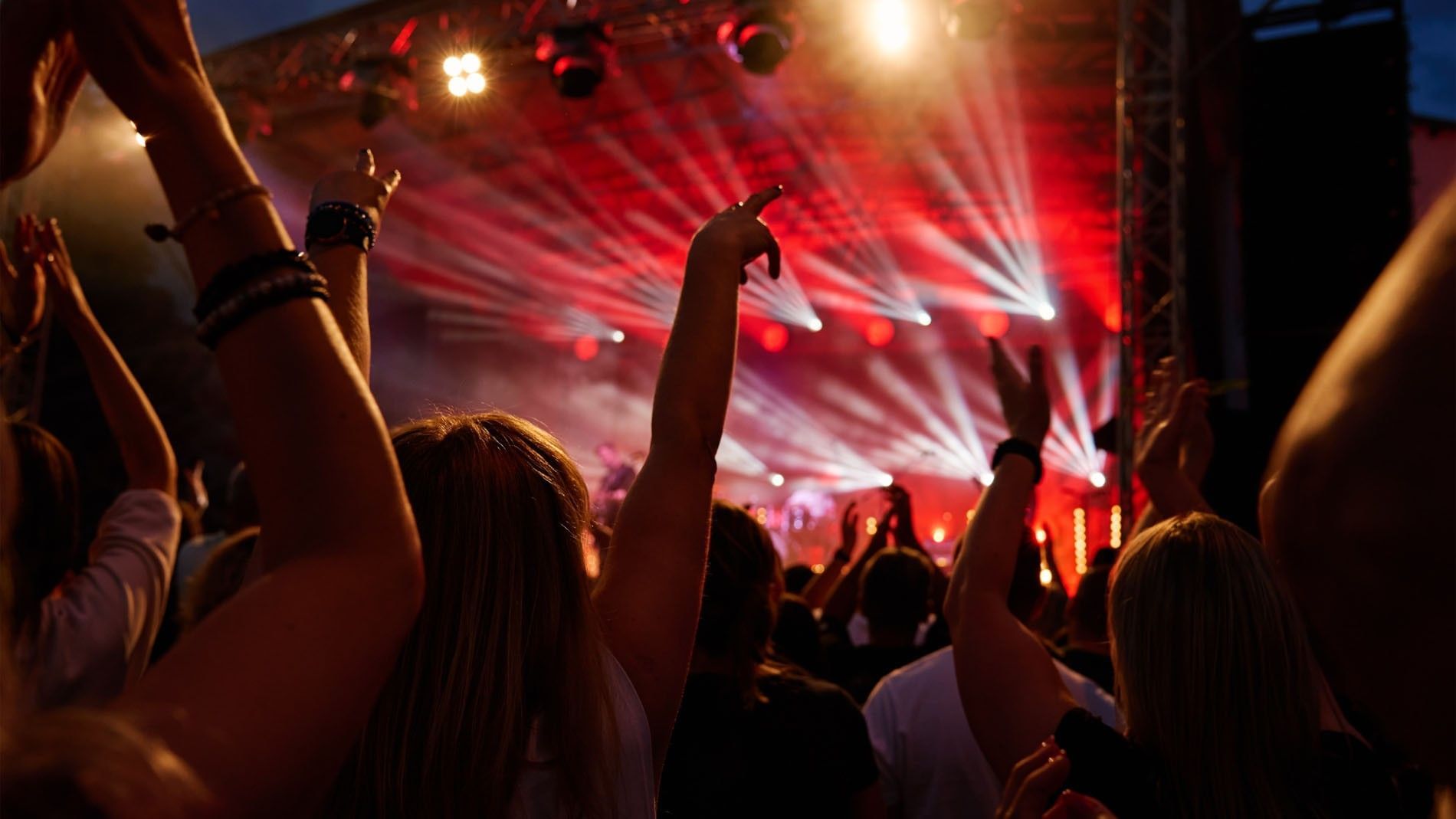 Enthusiastic crowd with raised hands at a live music concert with red lights at Camino Real Aeropuerto Mexico