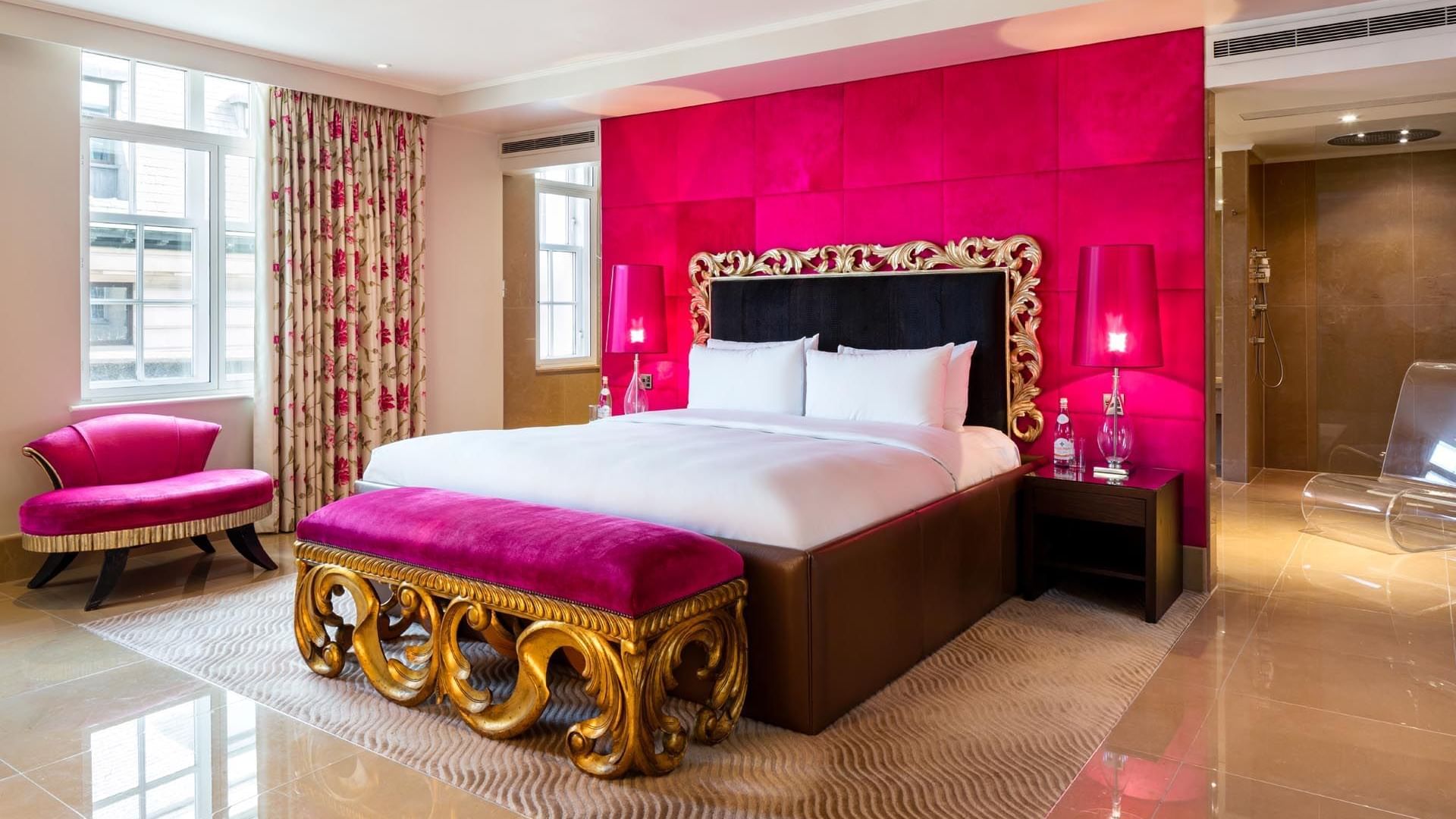 Luxurious Schiaparelli Suite at The May Fair Hotel London featuring a pink accent wall, plush bed, bench, and lamps
