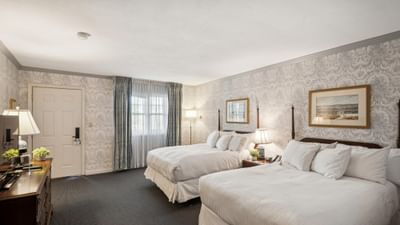Two beds near floor lamp and wooden dresser with television in guest room at Avon Old Farms Hotel