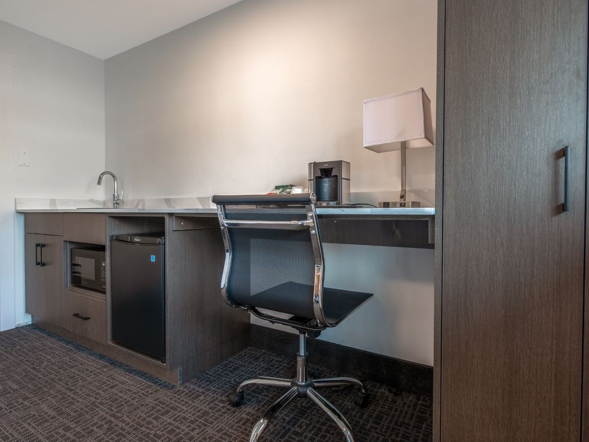 Hotel suite with a desk, chair, coffee maker, lamp, sink, and a toilet visible in the background.