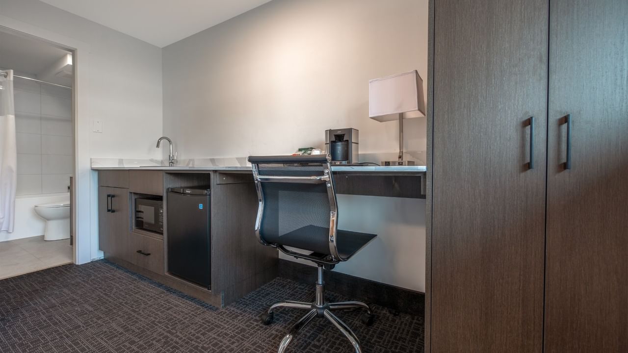 Hotel suite with a desk, chair, coffee maker, lamp, sink, and a toilet visible in the background.