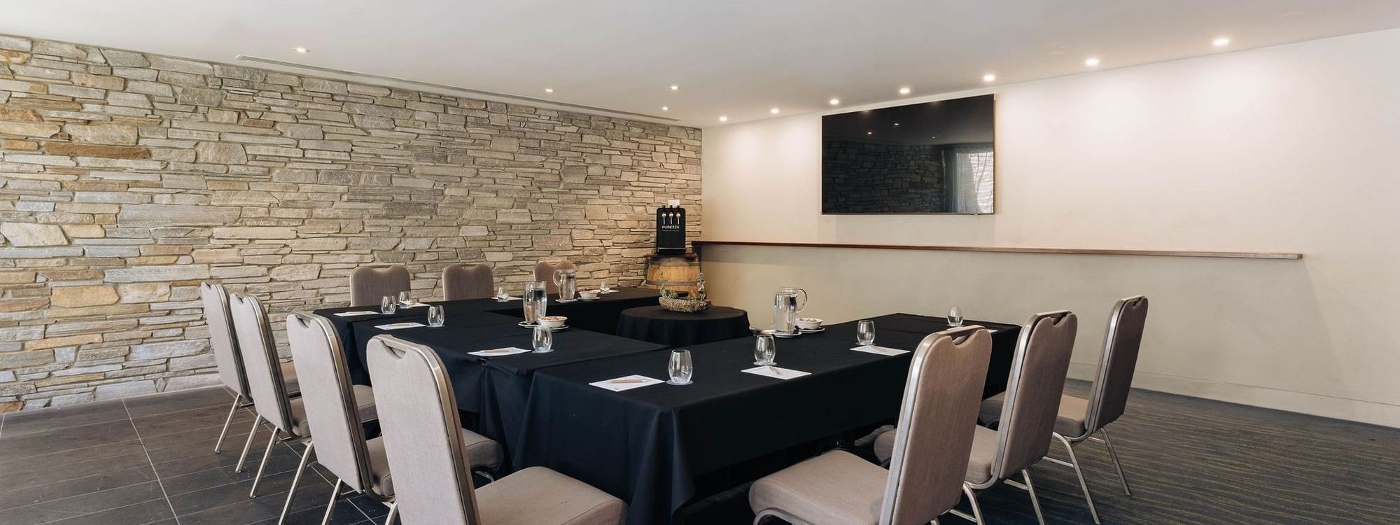Modern meeting room with stone accent wall, black-draped conference table, and upholstered chairs for Executive Retreat Package