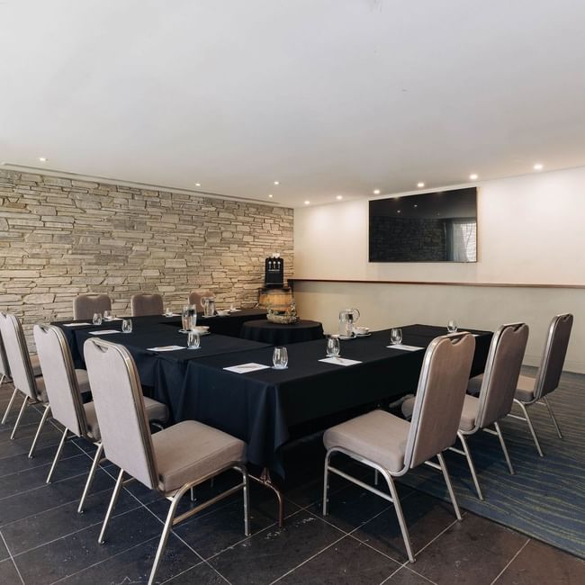Modern meeting room with stone accent wall, black-draped conference table, and upholstered chairs for Executive Retreat Package