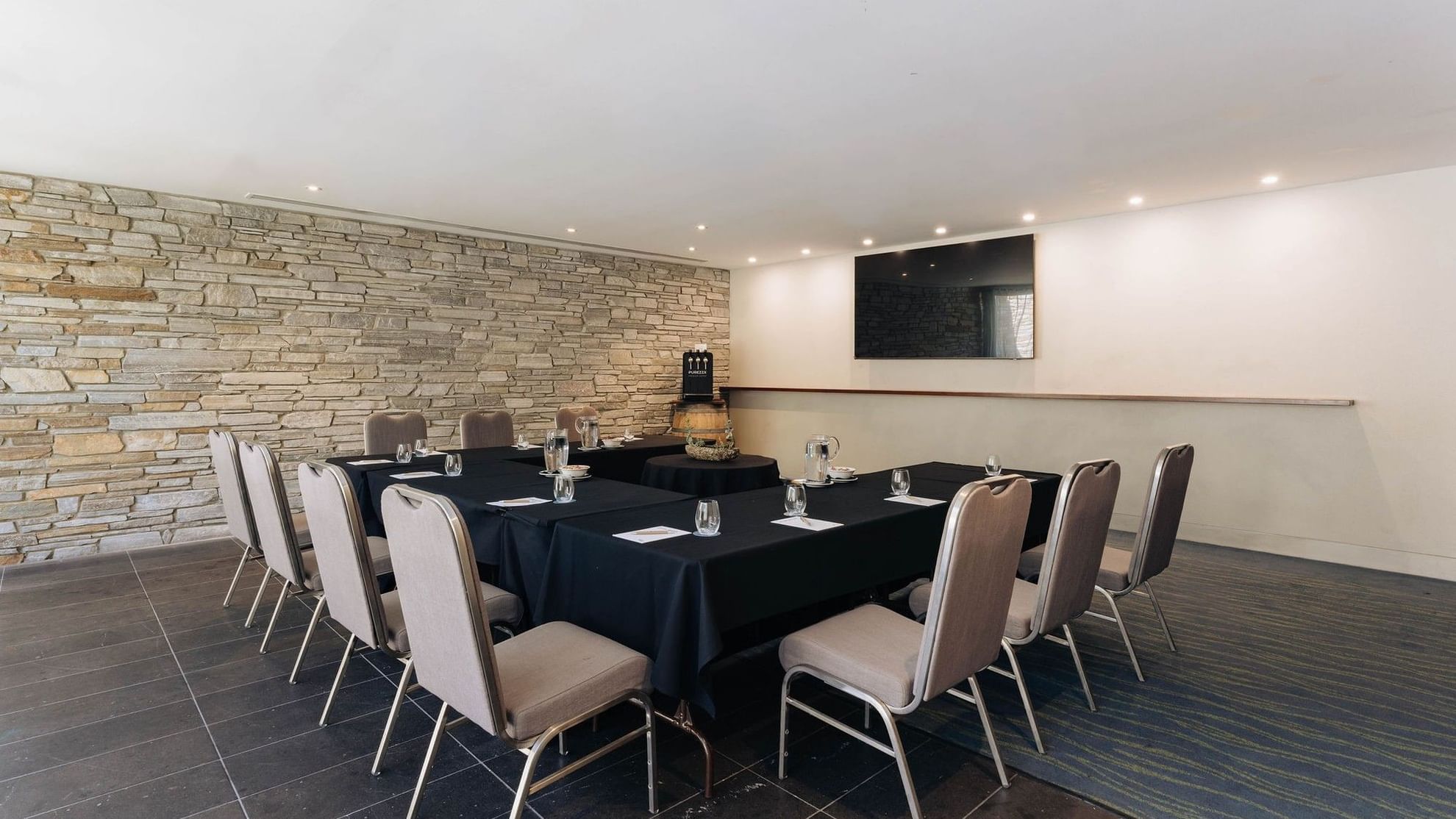 Modern meeting room with stone accent wall, black-draped conference table, and upholstered chairs for Executive Retreat Package