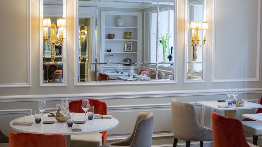 Le Céladon dining area featuring white tables placed by wall mirrors and gold sconces at Hotel Westminster Paris