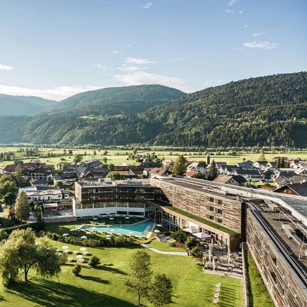 Aerial view of Falkensteiner Hotel & Spa Carinzia set amid lush green mountains under a blue sky