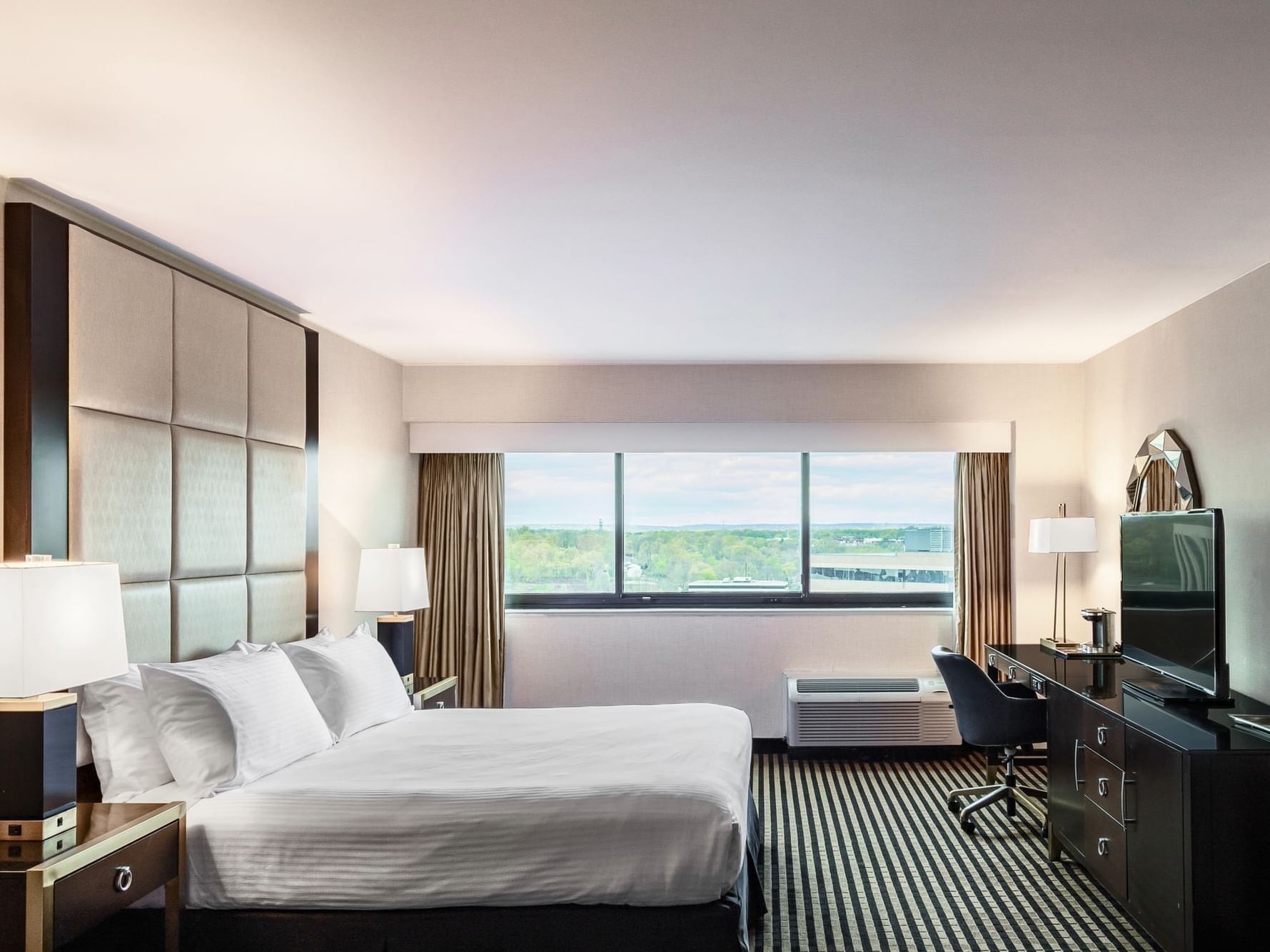 King Bed Room with white bedding, a desk, and a city view at APA Hotel Woodbridge in Iselin.