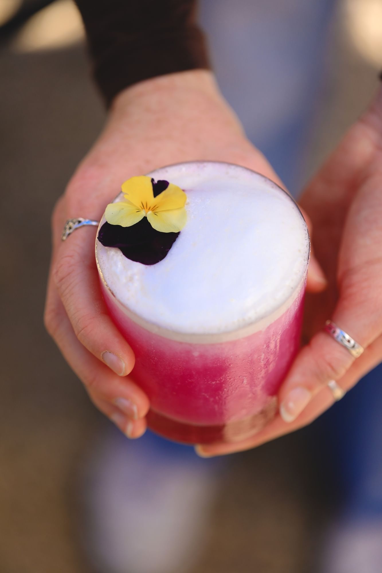 Lorem ipsum Hand holding a pink cocktail with white foam and yellow flower on top