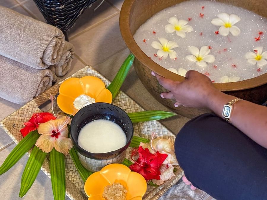Woman's hand reaching for a floral-filled wooden bowl, a bowl of milk, and tropical flowers at The Naviti Resort - Fiji.