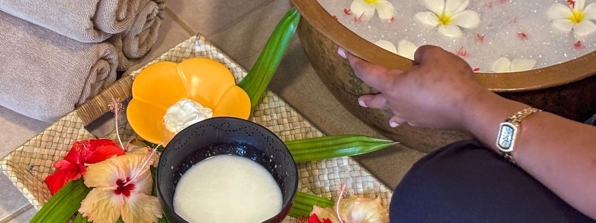 Person's hand reaching towards a wooden bowl filled with water and flowers at The Joy Spa in Korolevu