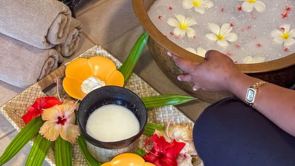 A person's hand reaching towards a wooden bowl filled with water and flowers at The Joy Spa in Korolevu.