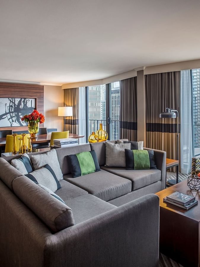 Emerald Suite 1908 with a large grey sectional sofa, dining area, and city skyline window views at Warwick Seattle