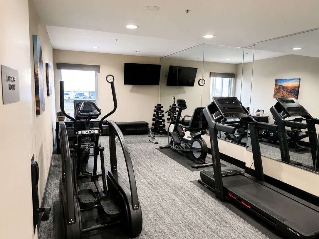 Modern fitness center with treadmills, elliptical, weights, mirrored wall, and TV at Booking - Boothill Inn