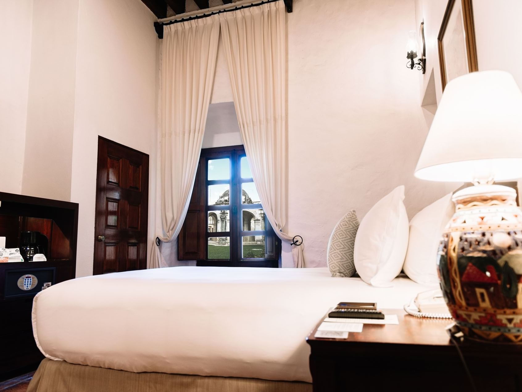 Queen Novicia Suite with a large bed, decorative pillows, and a lamp on a wooden nightstand at Quinta Real Oaxaca