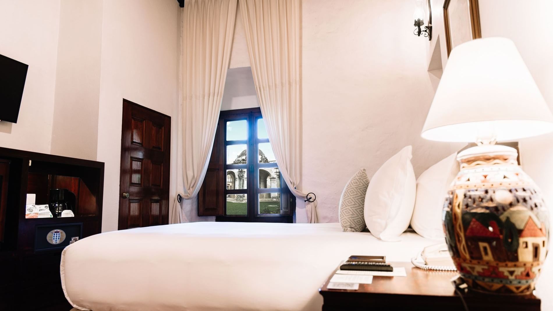 Queen Novicia Suite with a large bed, decorative pillows, and a lamp on a wooden nightstand at Quinta Real Oaxaca