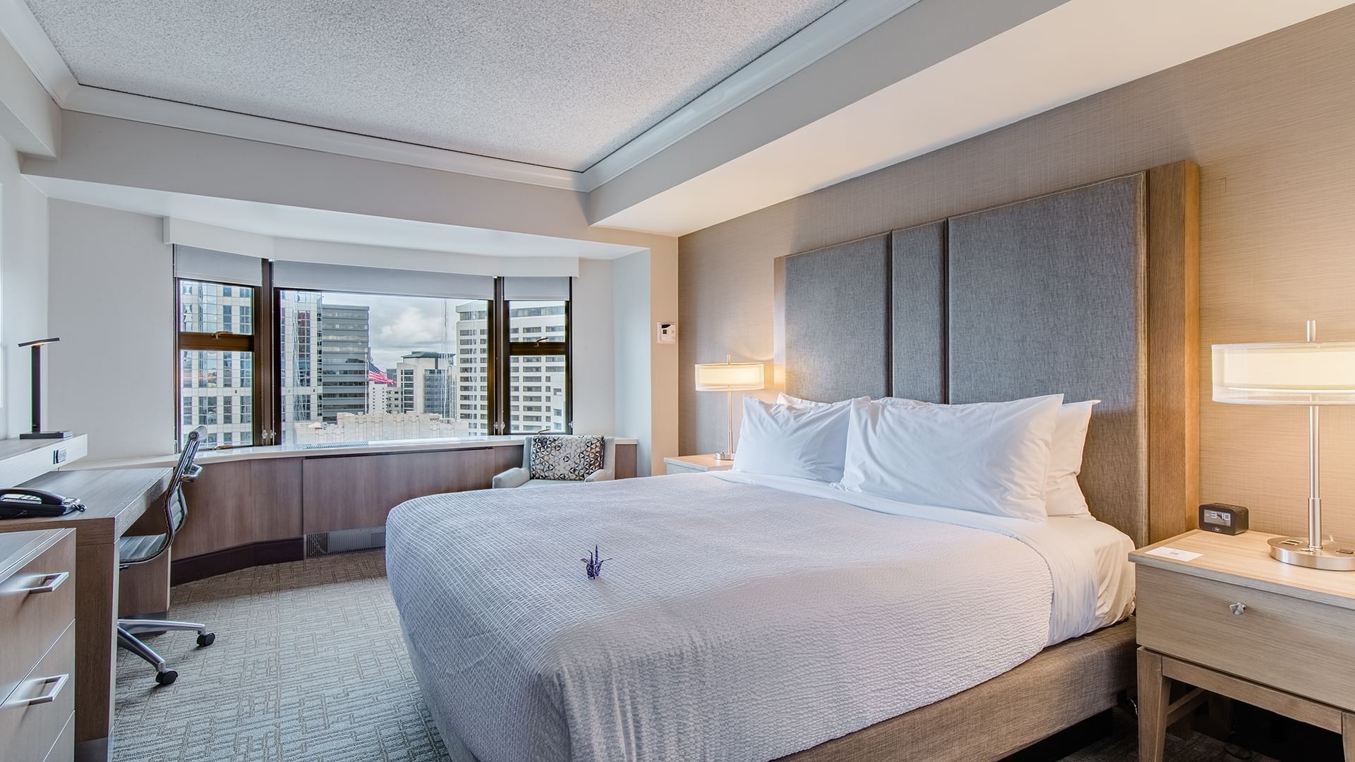A wide-angle view of a hotel room with a large bed, desk, and city view.