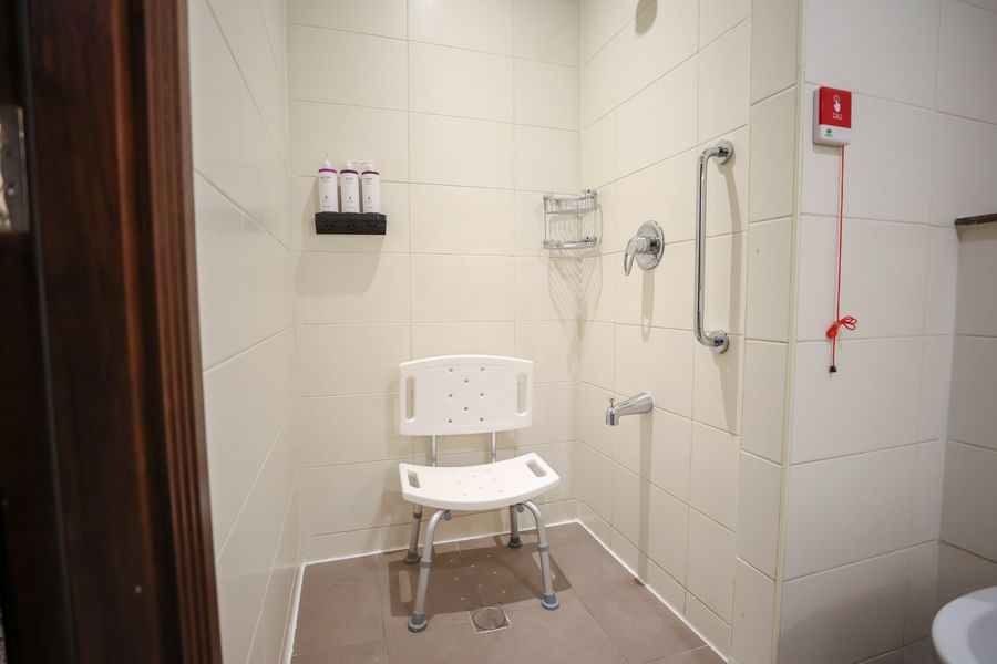 Accessible room bathroom featuring a white shower chair and grab bars with soap dispenser at Saja by Warwick Makkah