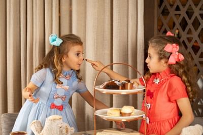 Two young girls in blue and coral dresses with matching hair bows enjoying afternoon tea at May Fair Kitchen