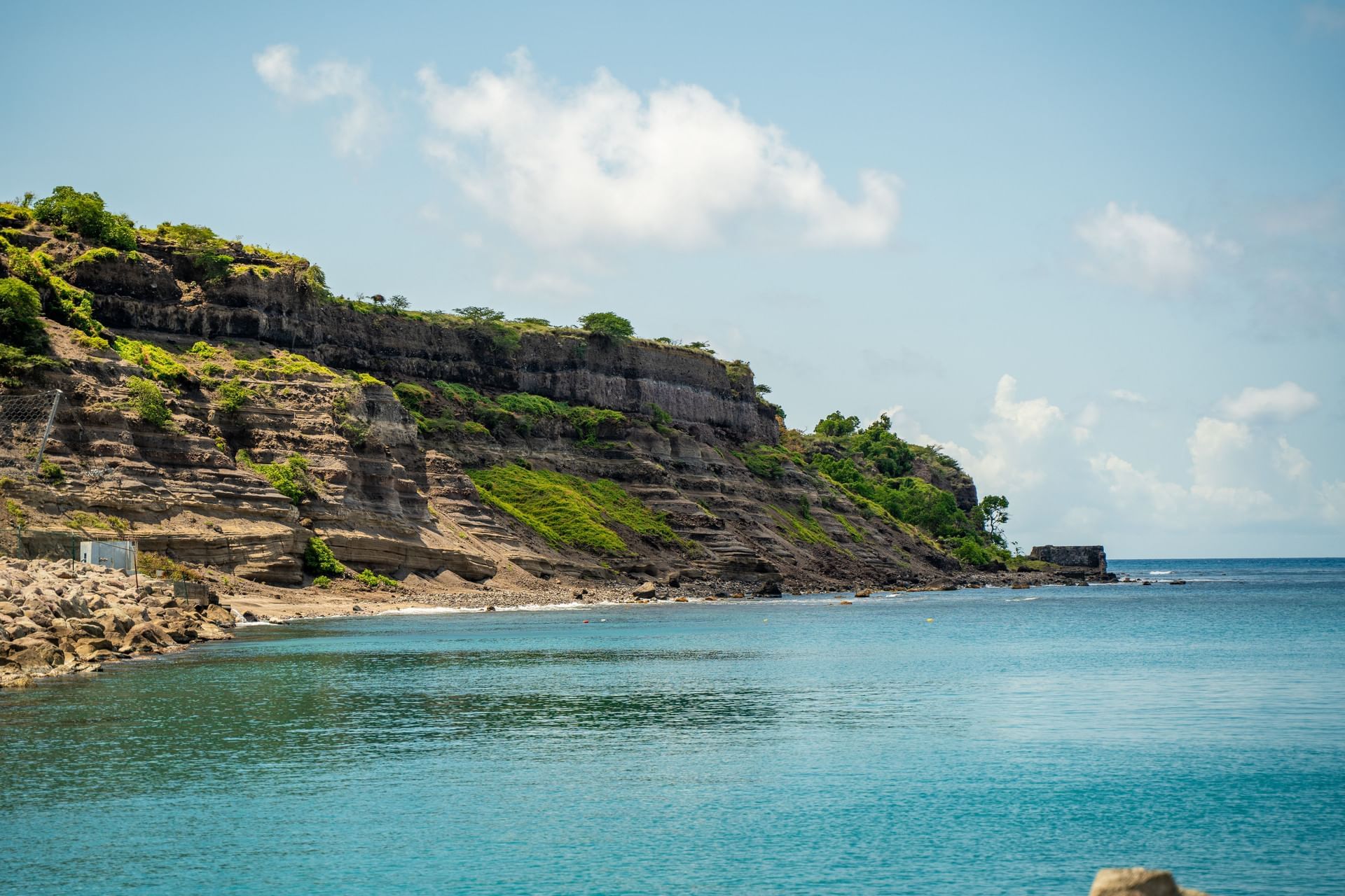 Serene coastal view of St. Eustatius along clear turquoise ocean waters near steep green hills at Golden Rock Resort