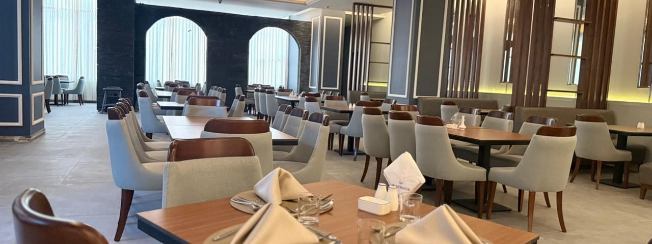 Set tables by grey chairs surrounding a large pillar in Almir Restaurant at Warwick Jeddah Hotel & Spa