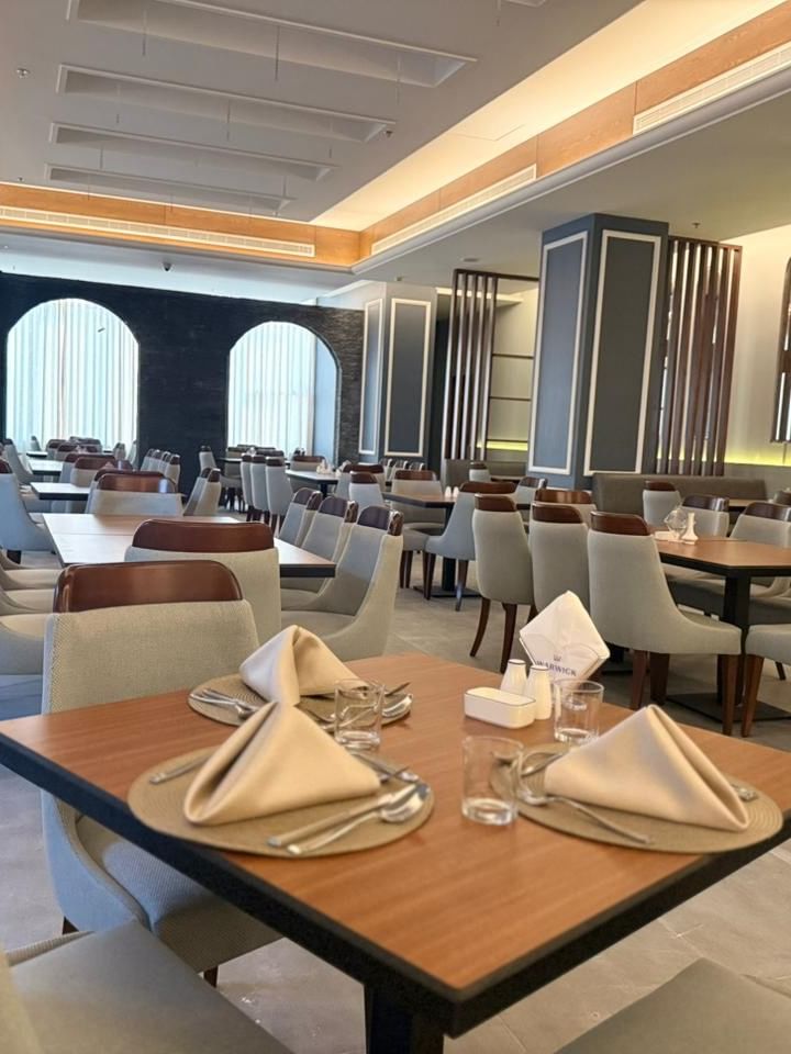 Set tables by grey chairs surrounding a large pillar in Almir Restaurant at Warwick Jeddah Hotel & Spa