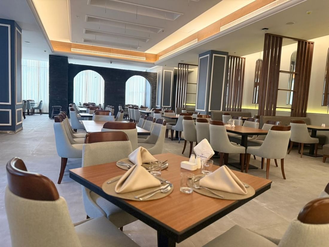 Set tables by grey chairs surrounding a large pillar in Almir Restaurant at Warwick Jeddah Hotel & Spa