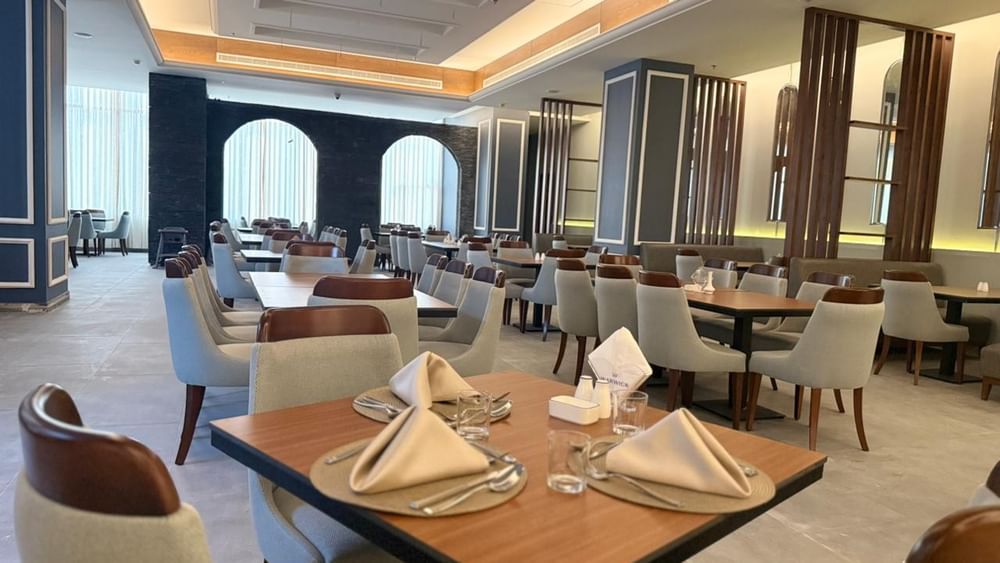 Set tables by grey chairs surrounding a large pillar in Almir Restaurant at Warwick Jeddah Hotel & Spa